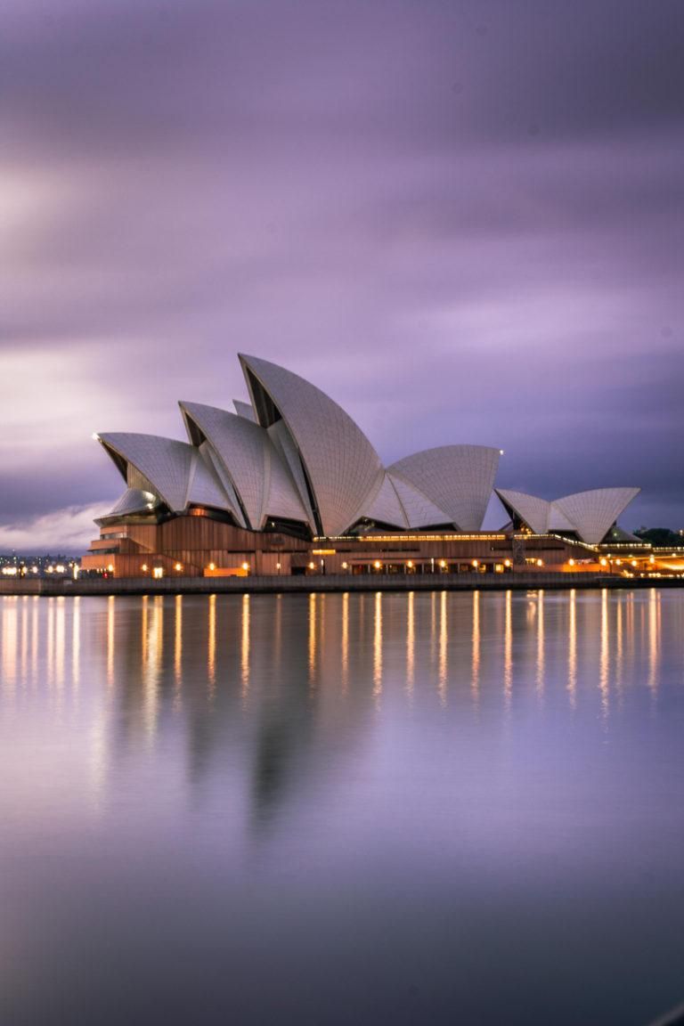 The Sydney Opera House reflected in the harbour under a purple dusk sky