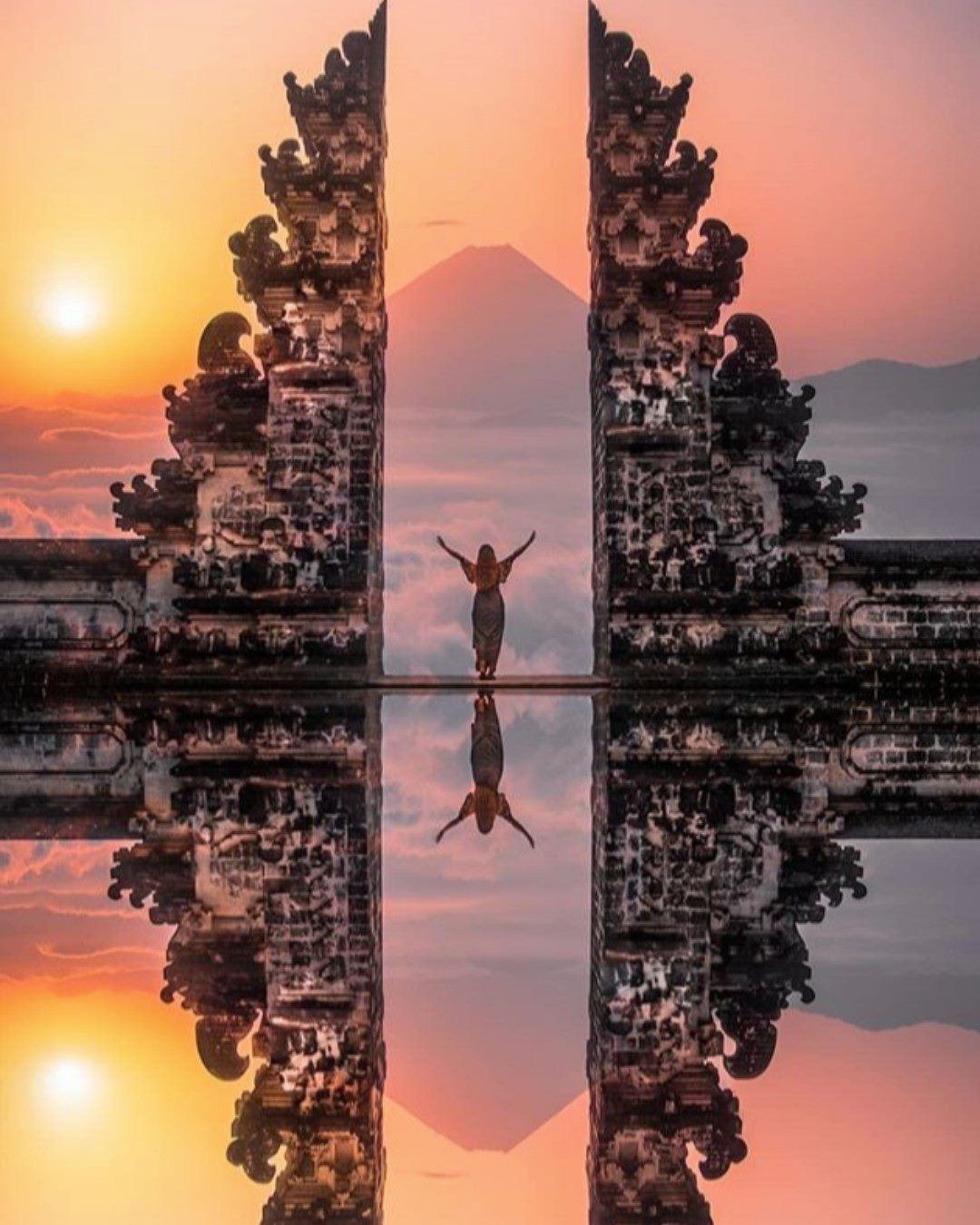 A traveller between the stone Gates of Heaven in Bali, reflected in still water at sunrise