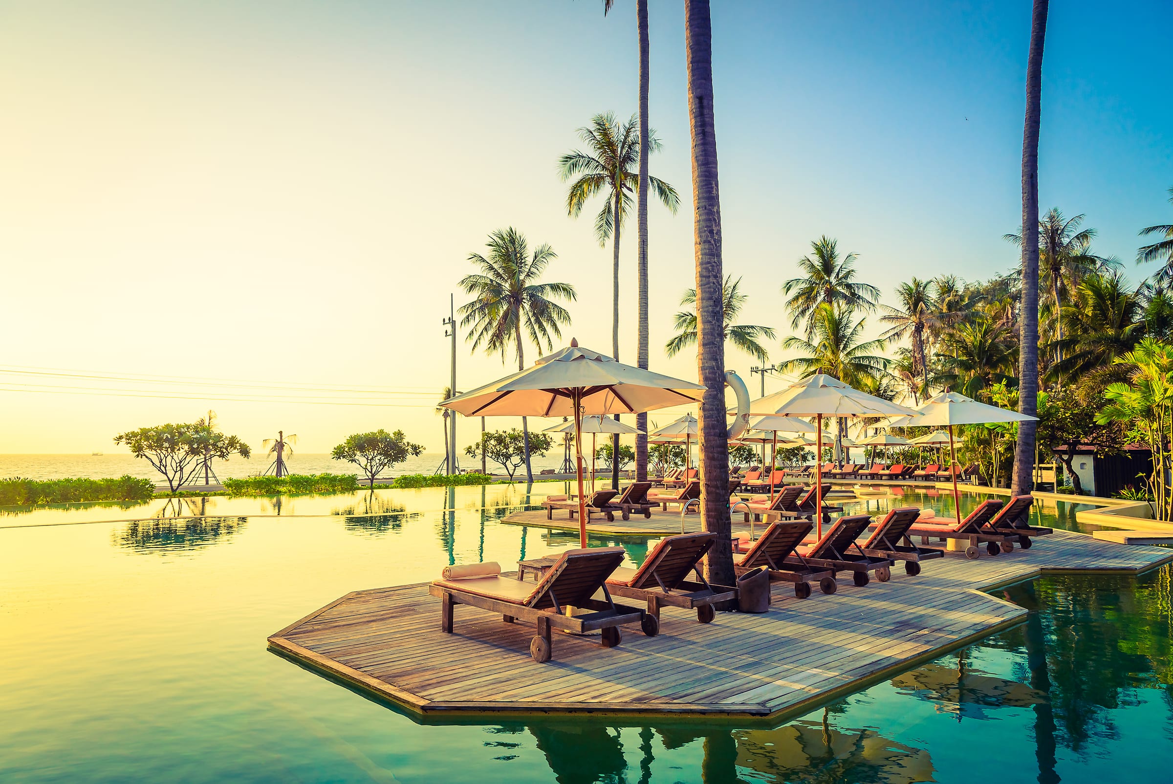 Palm trees and sun loungers beside an infinity pool overlooking the sea at sunrise