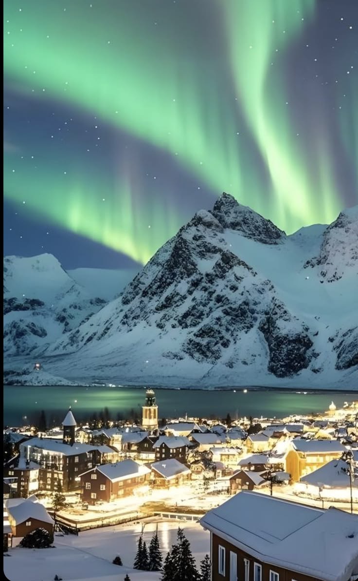 Green northern lights over snow-covered mountains and a lit-up winter town