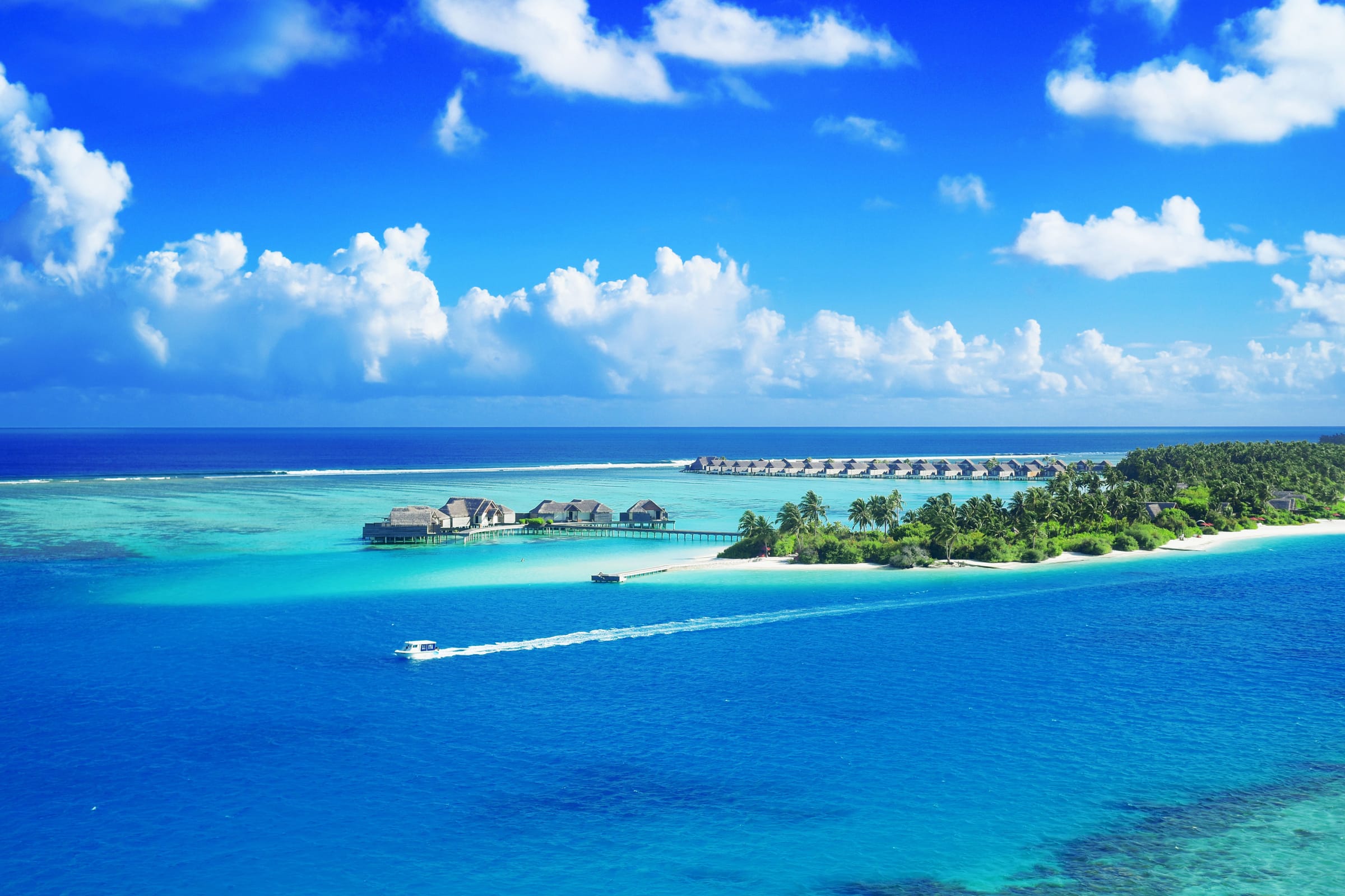 Overwater villas and a palm-fringed island in a turquoise lagoon, a speedboat crossing the sea