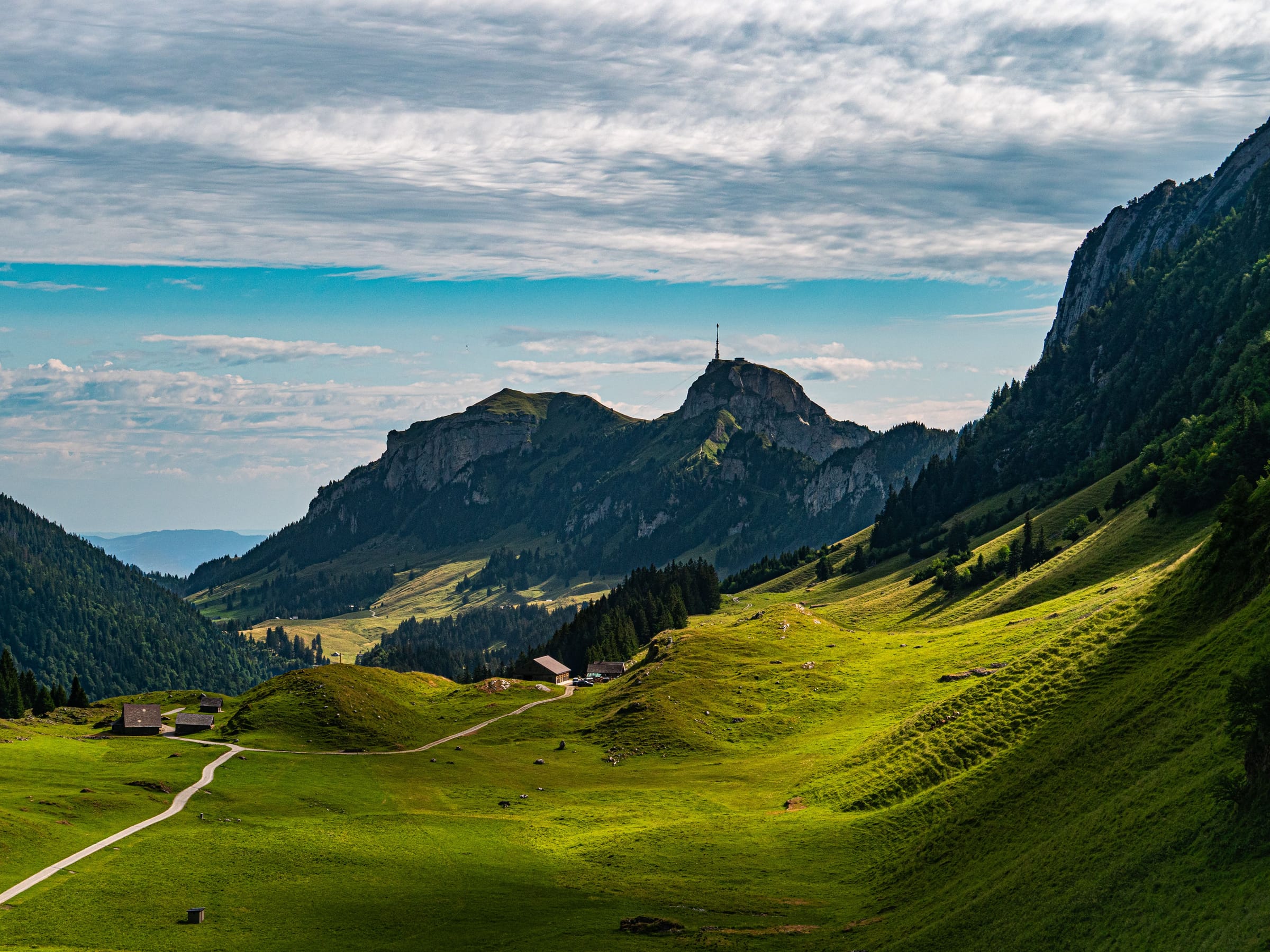 Green alpine meadows and chalets in a valley beneath a rocky peak