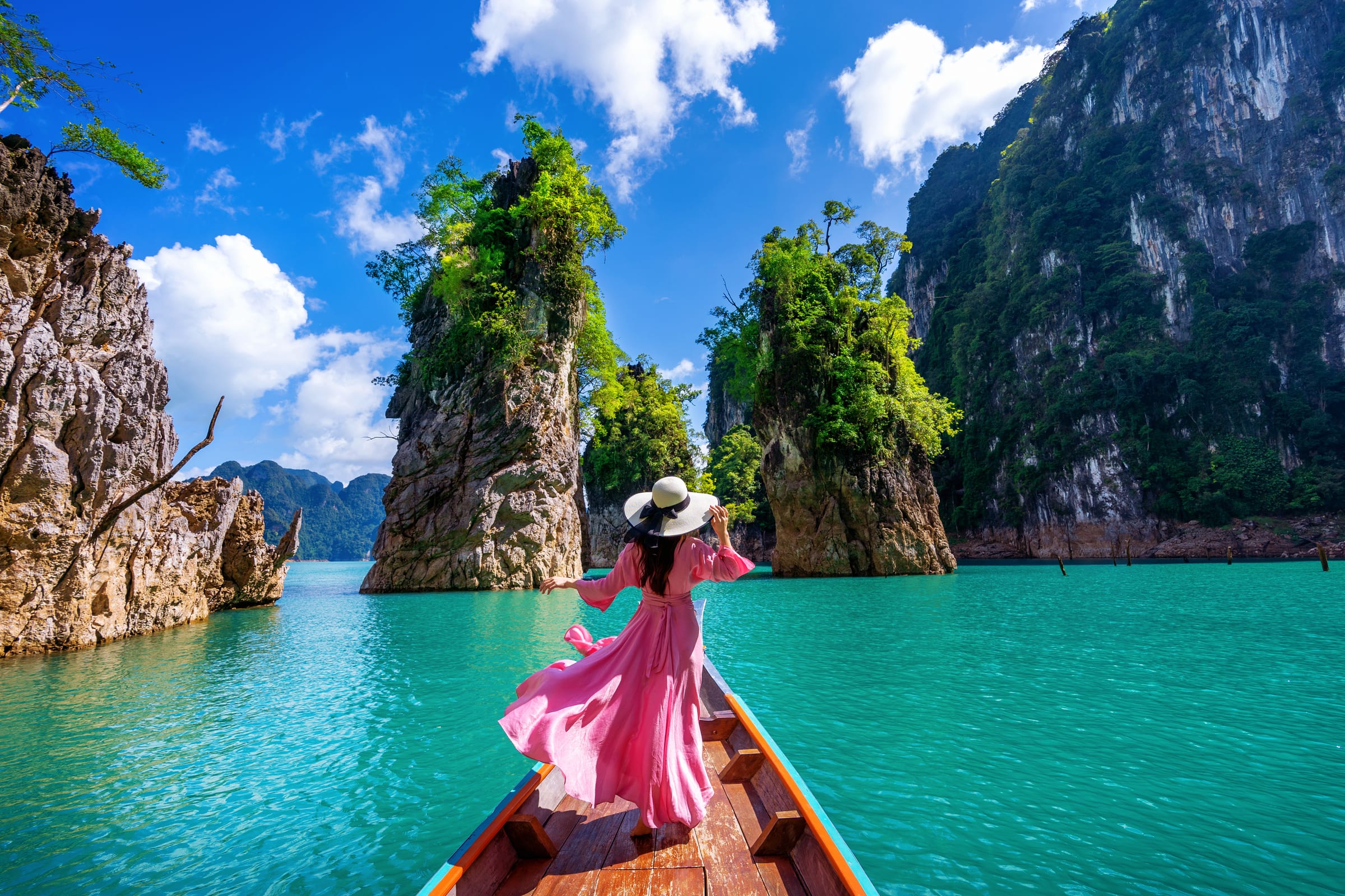 A traveller on a longtail boat among limestone cliffs on emerald water
