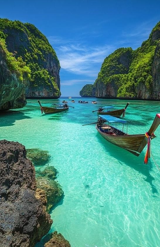 Longtail boats on turquoise water between green limestone cliffs in Thailand