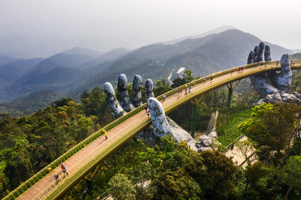 The Golden Bridge held up by two giant stone hands above forested mountains